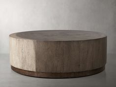 a round wooden table sitting on top of a cement floor next to a white wall