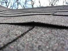 a close up view of the top of a shingled roof with trees in the background