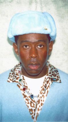 a man with a blue hat and leopard print shirt is posing for a photo in front of a white wall