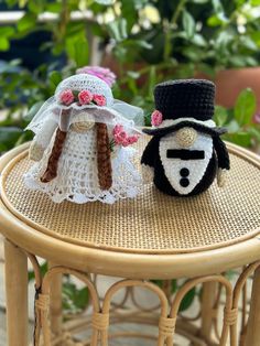 two wedding dolls sitting on top of a table next to each other in front of some plants