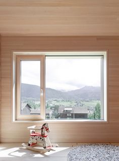 a rocking horse sits in front of a large window with mountains out the back ground