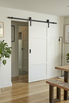 a room with a wooden table and white doors in the center, two planters on either side of the door