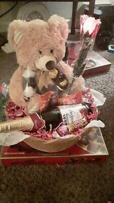 a teddy bear sitting on top of a box filled with chocolates and wine bottles