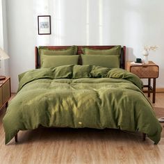 a bed with green comforter and pillows in a white room next to a lamp