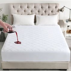 a person pouring red wine into a bed with white linens and pillows on it