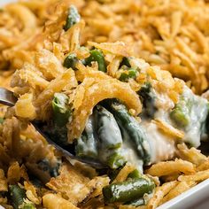 a spoon full of green bean casserole with cheese and onions on top, in a white dish