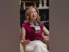 a woman is sitting in a chair with a microphone and talking into the camera while wearing a red shirt