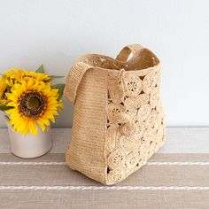 a crocheted bag next to a sunflower in a vase on a table