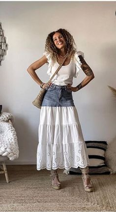 a woman standing in a room with her hands on her hips wearing a white top and denim skirt