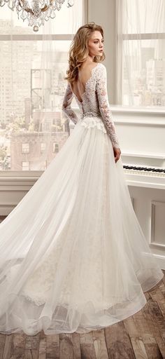 a woman standing in front of a white piano wearing a long sleeved wedding dress