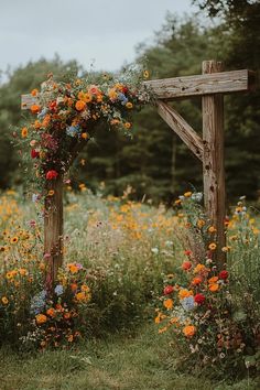 a wooden cross with flowers on it in the middle of some grass and trees behind it