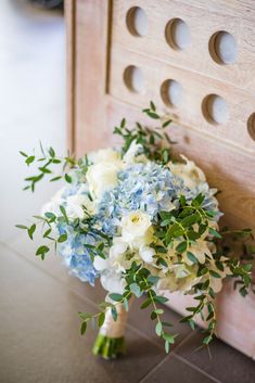 a bridal bouquet sitting on the floor next to a wooden door with holes in it