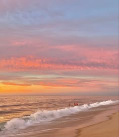 people walking on the beach at sunset with waves coming in to shore and pink clouds