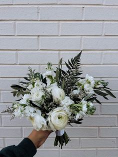 someone holding a bouquet of white flowers in front of a brick wall