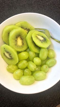 grapes and kiwi in a white bowl with a spoon