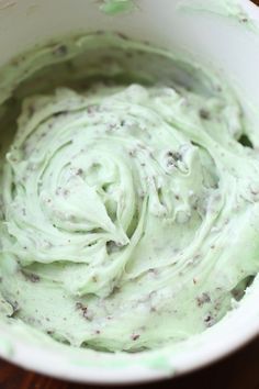 a white bowl filled with green frosting on top of a wooden table