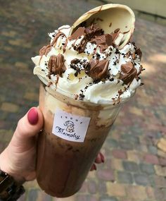 a person holding up an ice cream sundae with chocolate and whipped cream on top