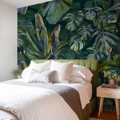 a bed with white sheets and pillows in front of a green tropical wallpaper