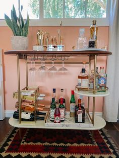 a bar cart filled with liquor bottles and glasses on top of a rug in front of a window