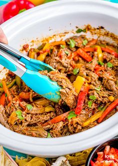 a person cutting into a shredded meat dish with tongs and vegetables in the background