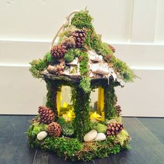 a small house made out of moss with pine cones and rocks on the outside, sitting on a wood floor