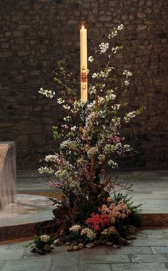 a tall candle with flowers and rocks on the ground