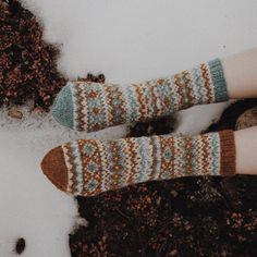 two feet wearing socks in the snow with their legs covered by knitted mitts