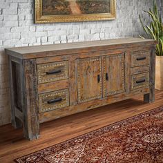 an old wooden cabinet in front of a brick wall with a painting on the wall