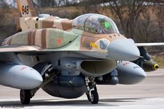 a fighter jet sitting on top of an airport tarmac with trees in the background