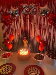 a woman sitting in front of a cake with lit candles on it and balloons behind her