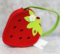 a red purse with a green strap and a white flower on the side, sitting on a plain surface