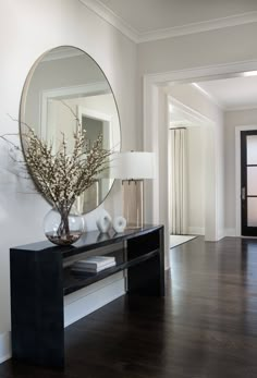 a large mirror on the wall above a black table with vases and flowers in it