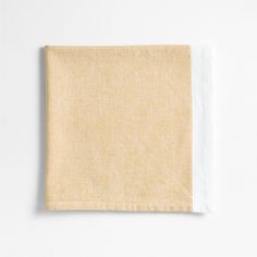 a folded napkin on a white surface with a light colored linen material in the corner