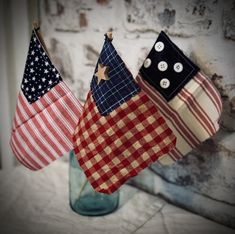 three american flags are hanging from clothes pins in a mason jar on a brick wall