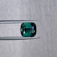 a green diamond being held by a pair of tongs