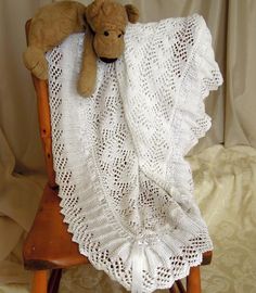 a teddy bear laying on top of a white crocheted blanket draped over a wooden chair