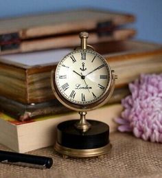 there is a small clock on top of a table next to some books and a pen