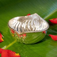 a silver bowl sitting on top of a green leaf covered in red flowers and petals