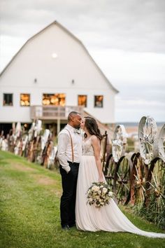 a bride and groom standing in front of a white barn with windmills on the grass