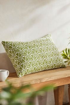 a green and white pillow sitting on top of a wooden bench next to a plant