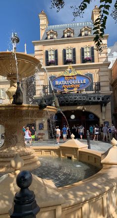 a fountain in front of a building with people walking around it