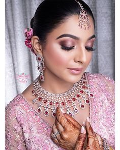 a woman in a pink dress with jewelry on her head and hands clasped together, looking at the camera