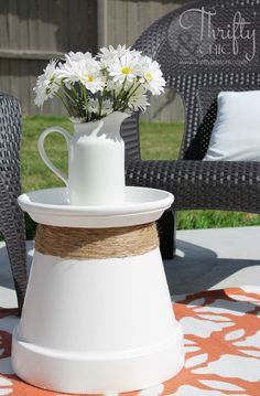 a white vase with daisies in it sitting on a patio table next to two wicker chairs