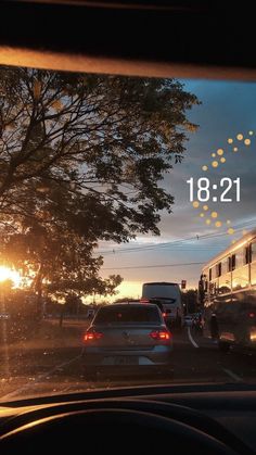 the sun is setting behind two cars driving down the road in front of a bus