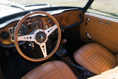 the interior of an old car with brown leather seats and steering wheel, along with wood dash boards