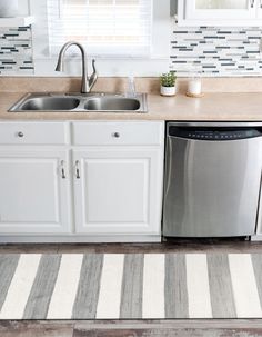 a clean kitchen with white cabinets and stainless steel dishwasher in the center, striped rug on the floor