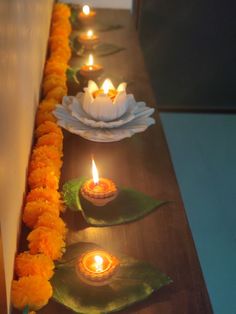 candles are lined up on a table with flowers and leaves around them, along with other decorations