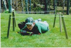 a young boy laying on the ground in front of some wooden poles and grass with trees behind him