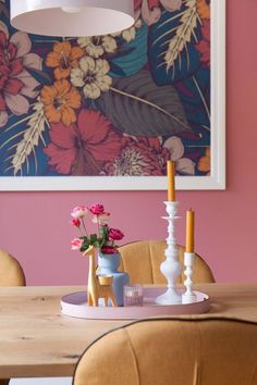 a dining room table with two candles on it and flowers in vases next to the candle holder