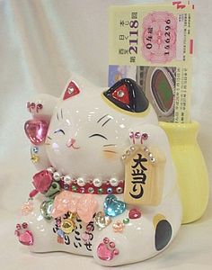 a white cat figurine next to a yellow vase with chinese characters on it